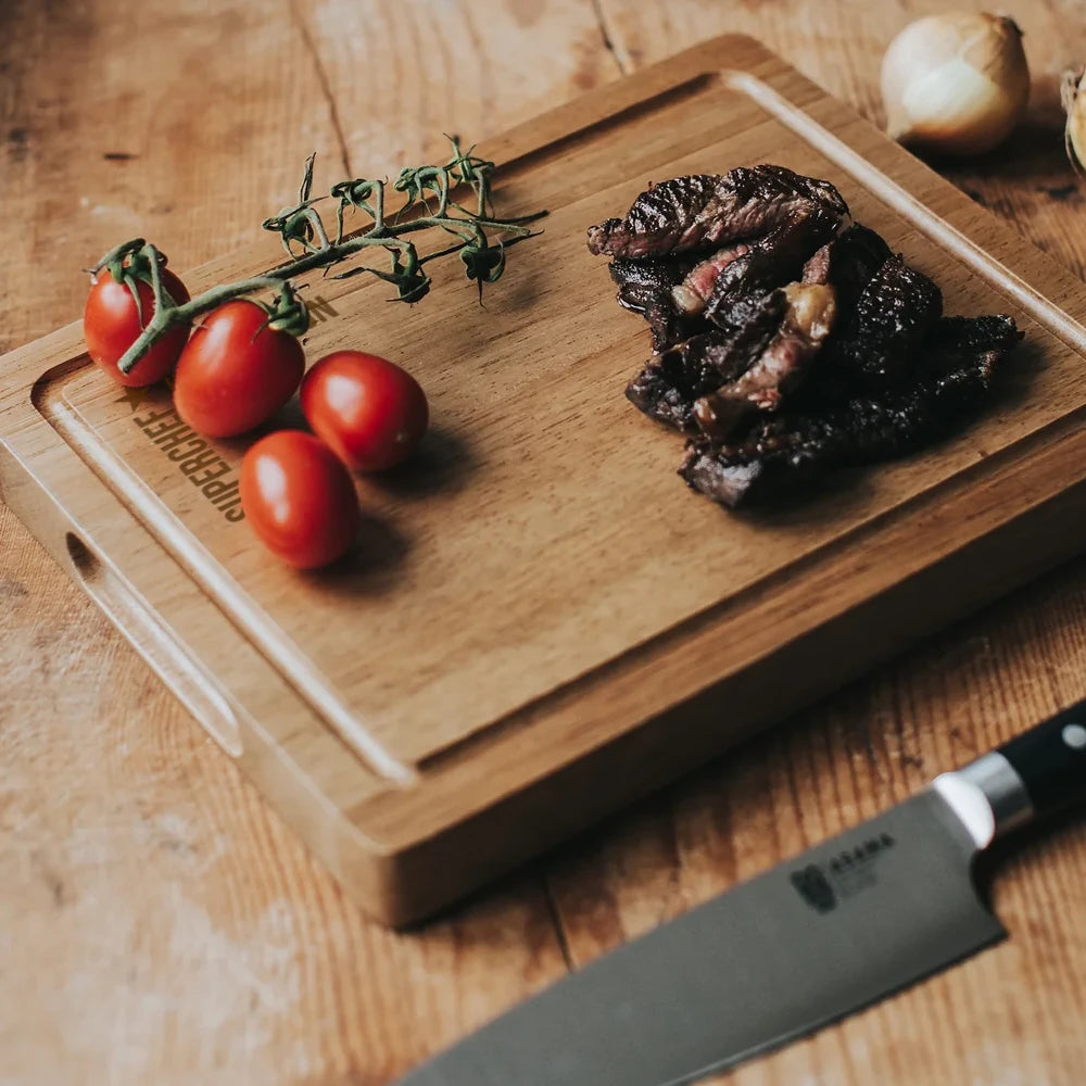 Graverad skärbräda i akacia med tomater och kött, och en kniv från Dorre i förgrunden