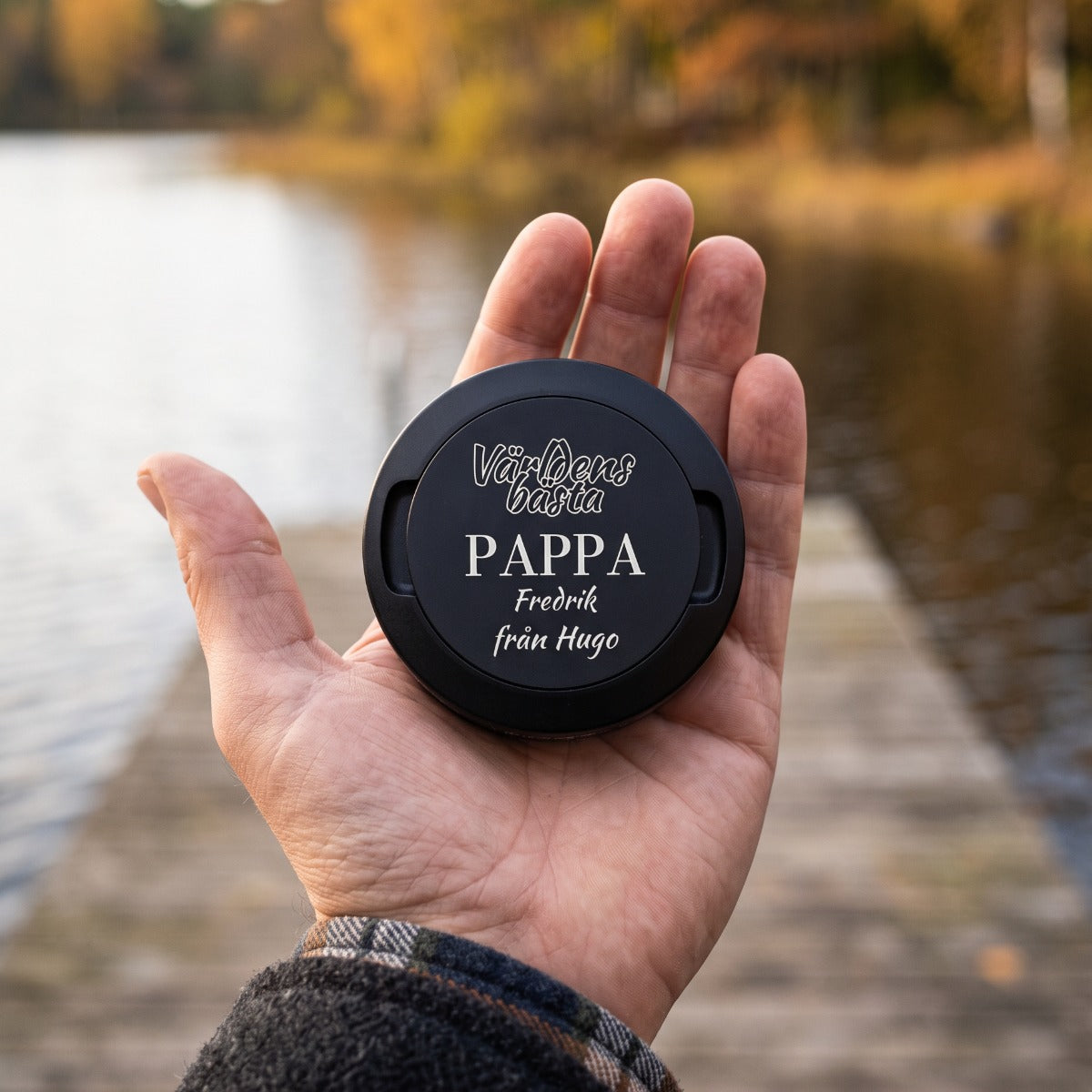 Man håller graverad snusdosa Världens bästa pappa i handen vid en brygga